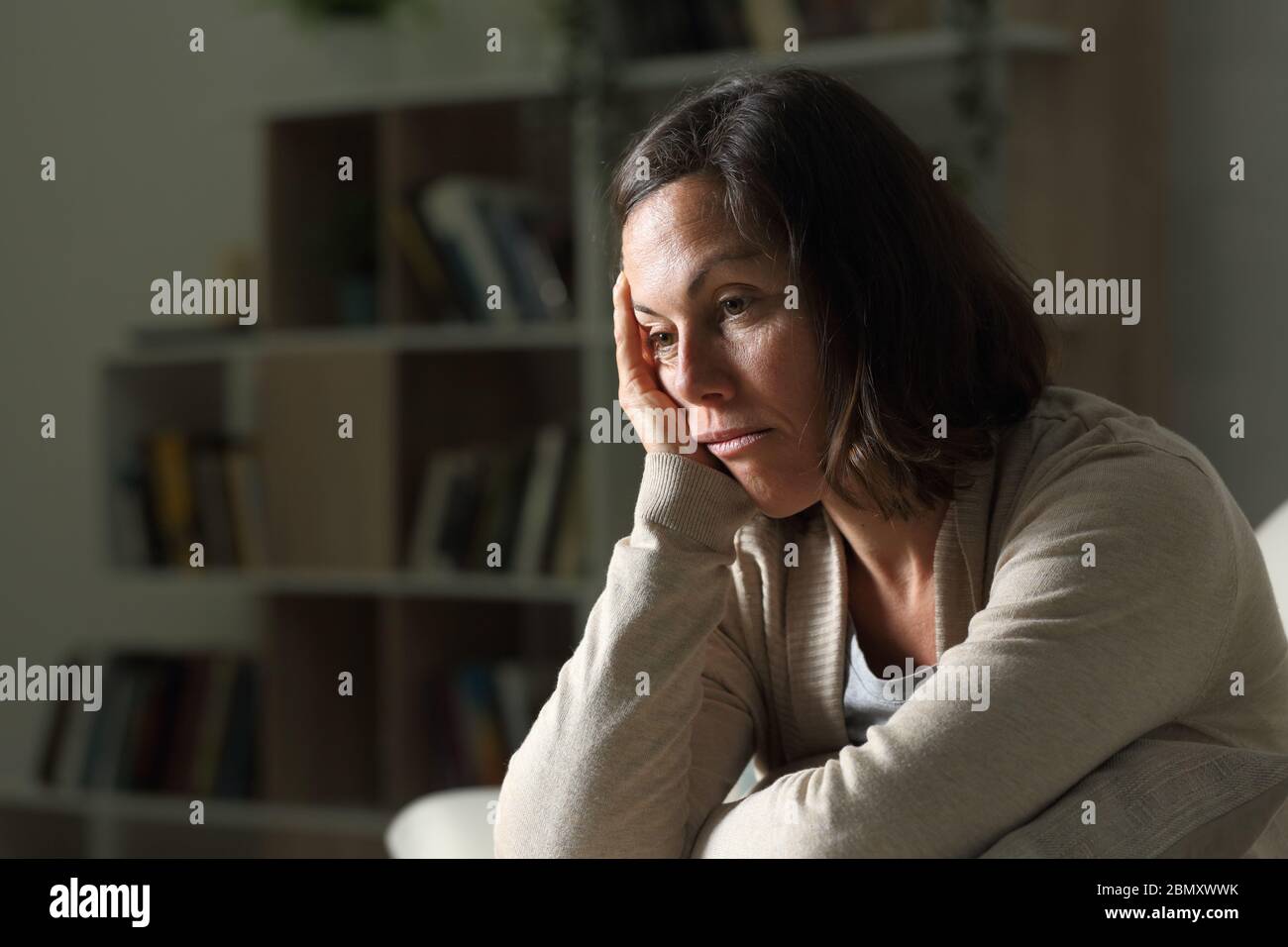 Gelangweilte Erwachsene Frau schaut weg auf dem Sofa in der Nacht zu Hause sitzen Stockfoto