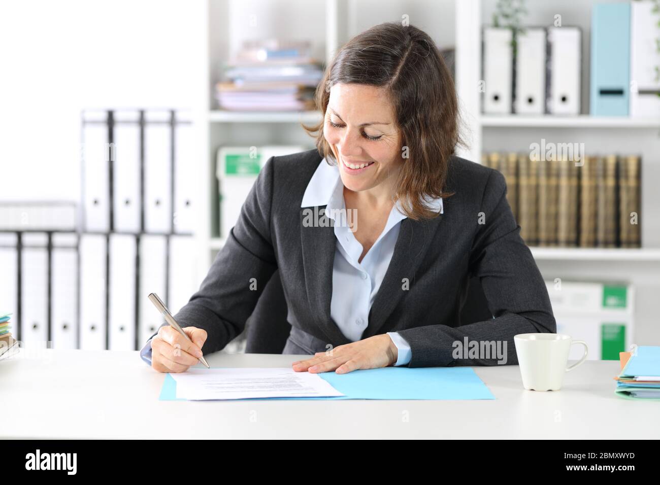 Glückliche Exekutive Dame Unterzeichnung Vertrag sitzt auf einem Schreibtisch im Büro Stockfoto
