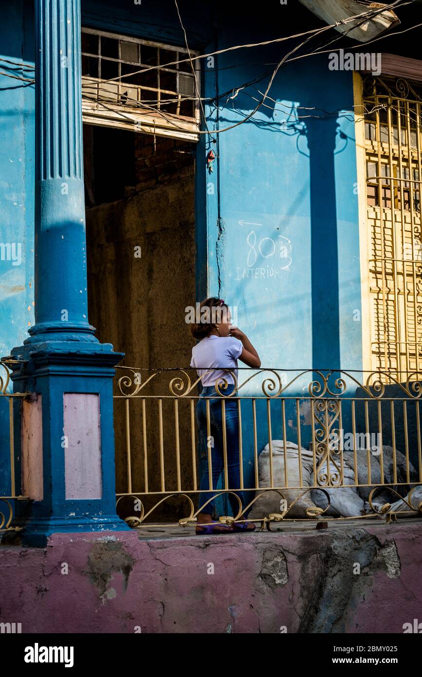 Mädchen auf Veranda in einer typischen Straße mit historischen Gebäuden im Stadtzentrum, Santiago de Cuba, Kuba Stockfoto