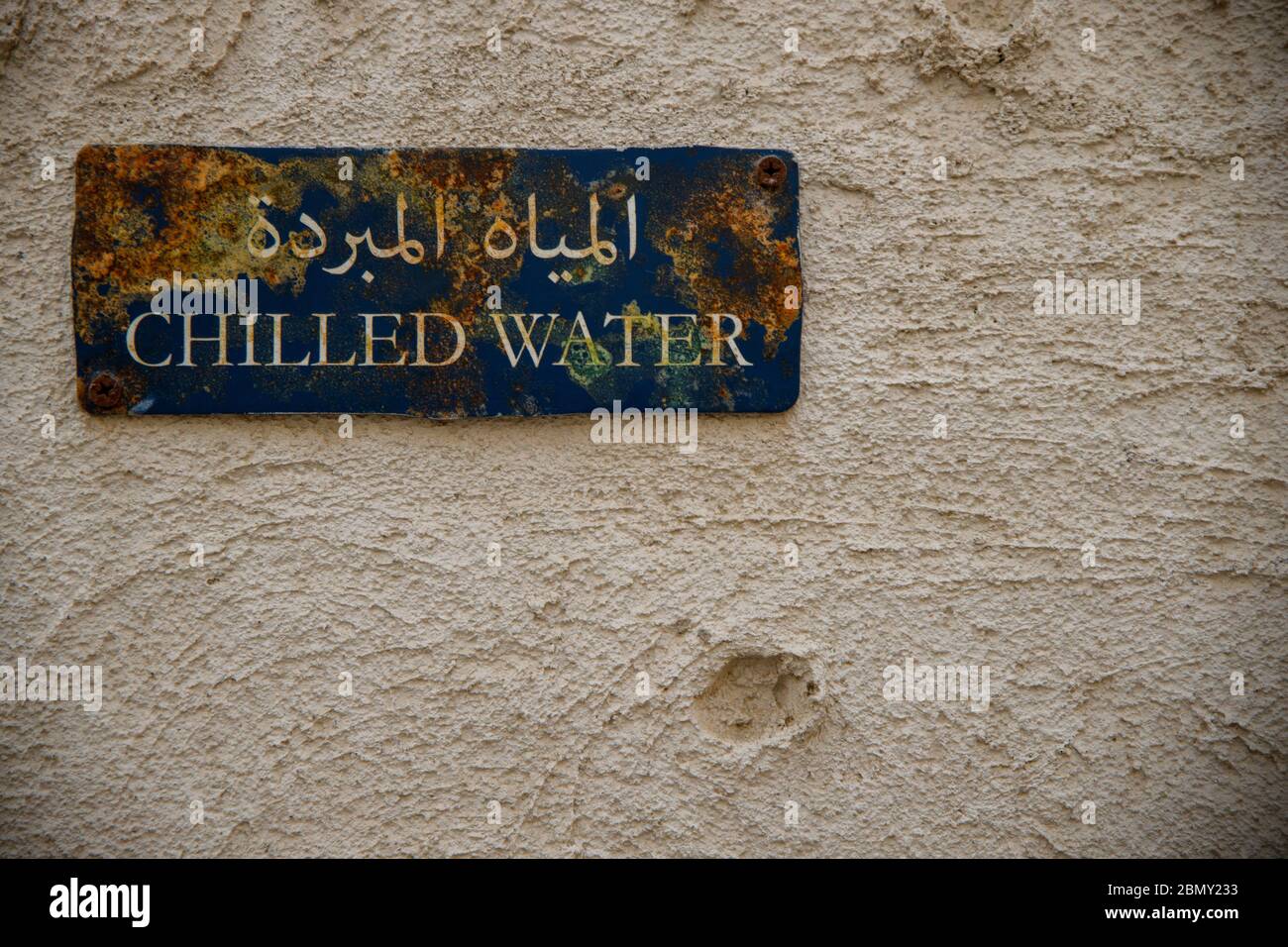 Altes Schild mit kaltem Wasser und Rost. Auf einem rostenden blauen Schild auf einem traditionellen arabischen Haus steht auf arabischer Schrift "Kaltwasser". Stockfoto