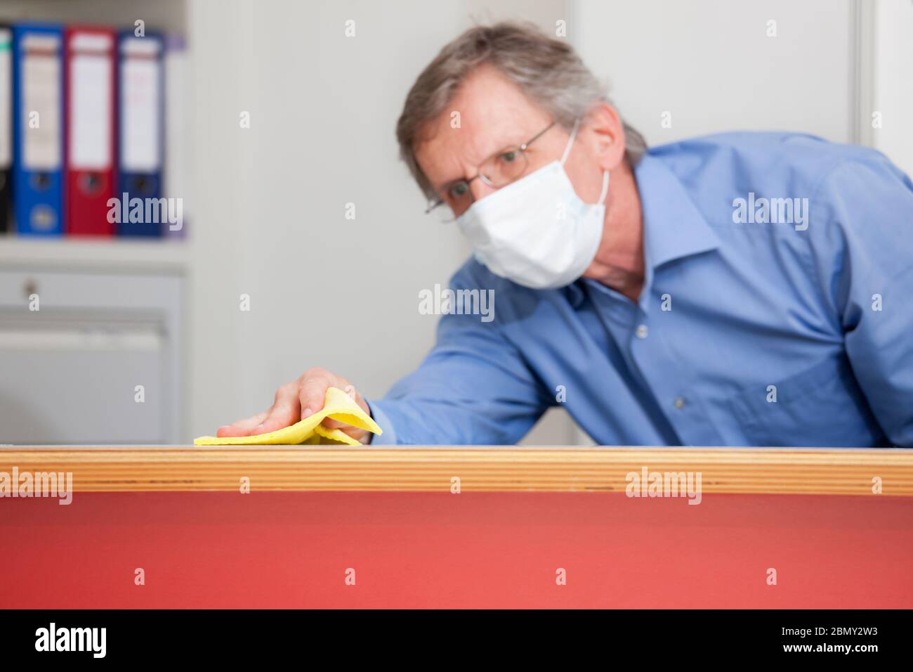 Reifer Geschäftsmann mit medizinischer Maske Reinigung eines Schreibtisches in einem Büro wegen Coronavirus - Fokus auf die Hand Stockfoto
