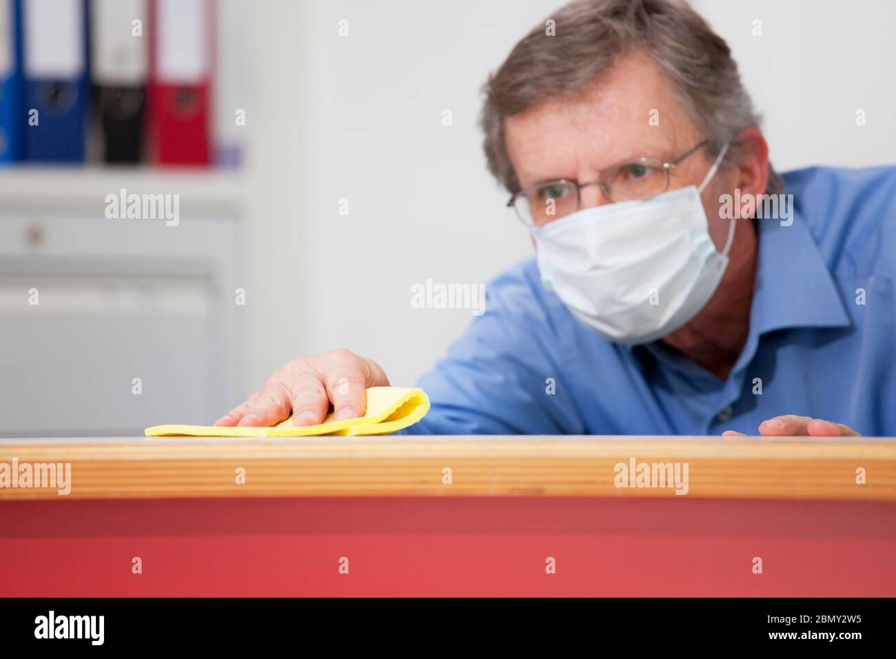 Reifer Geschäftsmann mit medizinischer Maske Reinigung eines Schreibtisches in einem Büro wegen Coronavirus - selektiver Fokus auf die Hand Stockfoto