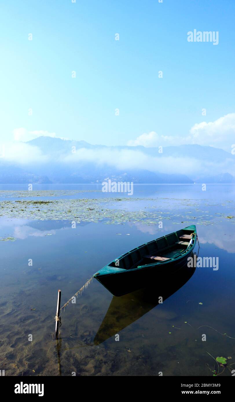 Ein einsames Holzboot schwimmt an einem nebligen Morgen auf dem Phewa See, Pokhara. Stockfoto
