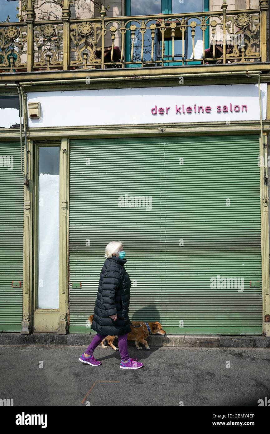 Wien, Österreich-April,20-2020: Ältere Frauen mit Schutzmaske gehen mit einem Hund und passieren einen geschlossenen Vintage-Shop mit dem Namen des Shops in Keim geschrieben Stockfoto