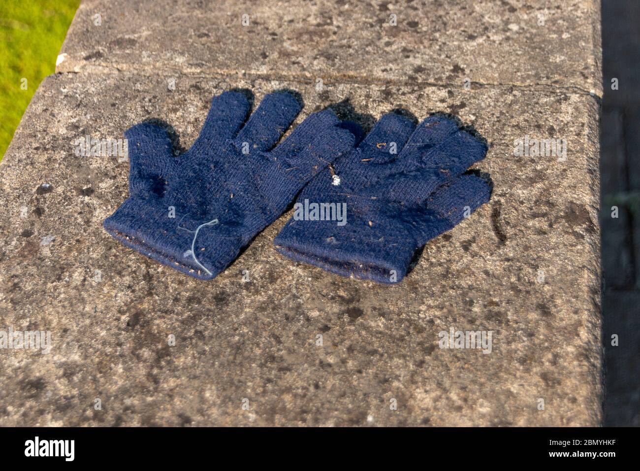 Eine Nahaufnahme eines kleinen, blauen Kinderhandschuhs, das an der Steinwand vor einem Haus zurückgelassen wurde Stockfoto