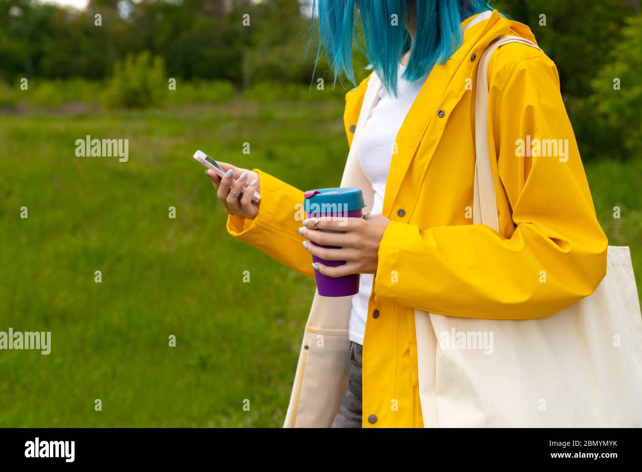 Junge Erwachsene schöne Frau mit blauen Haaren im Garten im Freien mit einem wiederverwendbaren Tasse mit heißem Getränk stehen Stockfoto