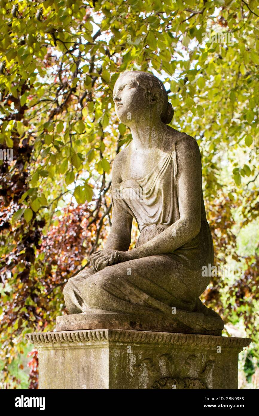 Statue eines jungen Mädchens auf einem Grabstein mit einem Bildschirm aus Buchenblättern aus Kupfer auf dem Brompton Cemetery, Kensington, London. Stockfoto