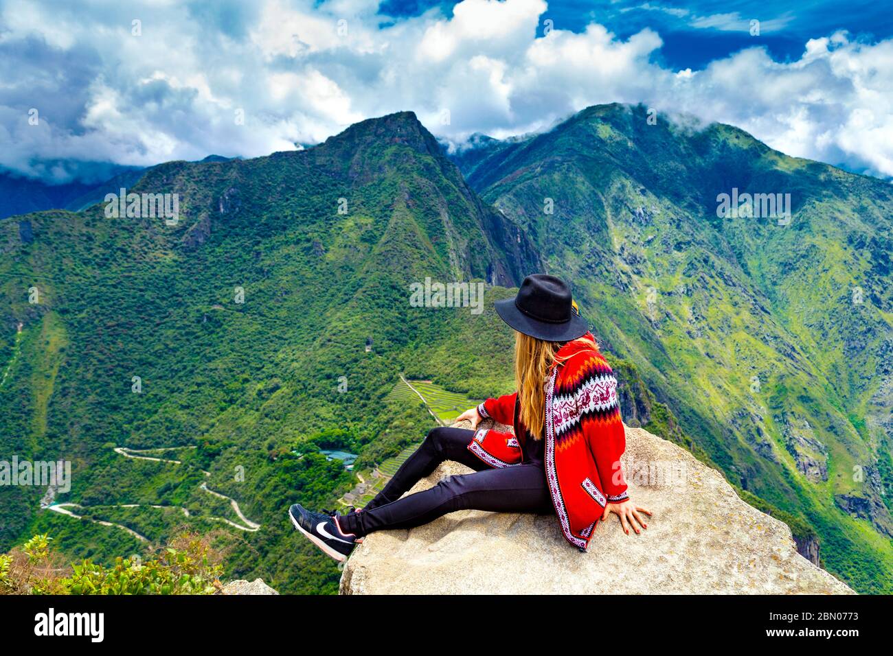Mädchen sitzt am Rand eines Felsens auf der Spitze von Huayna Picchu, landschaftlich schöne Aussicht über Machu Picchu und das Heilige Tal, Peru Stockfoto