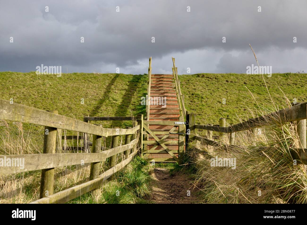Holzzaun bezeichnet Weg durch ein Naturschutzgebiet in Lincolnshire Fens in Richtung Stufen über die Meeresmauer in sich zusammenziehenden Wolken Stockfoto
