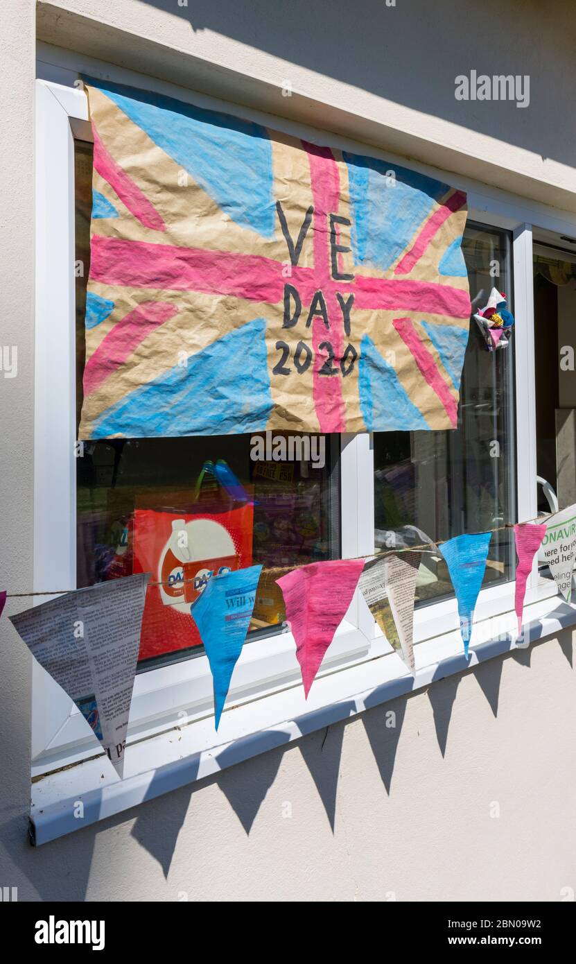 Bunte hausgemachte Union Jack Flagge und Bunting zum VE Day, 8. Mai 2020, an der Wand und Fenster eines Hauses in Surrey, Südostengland Stockfoto