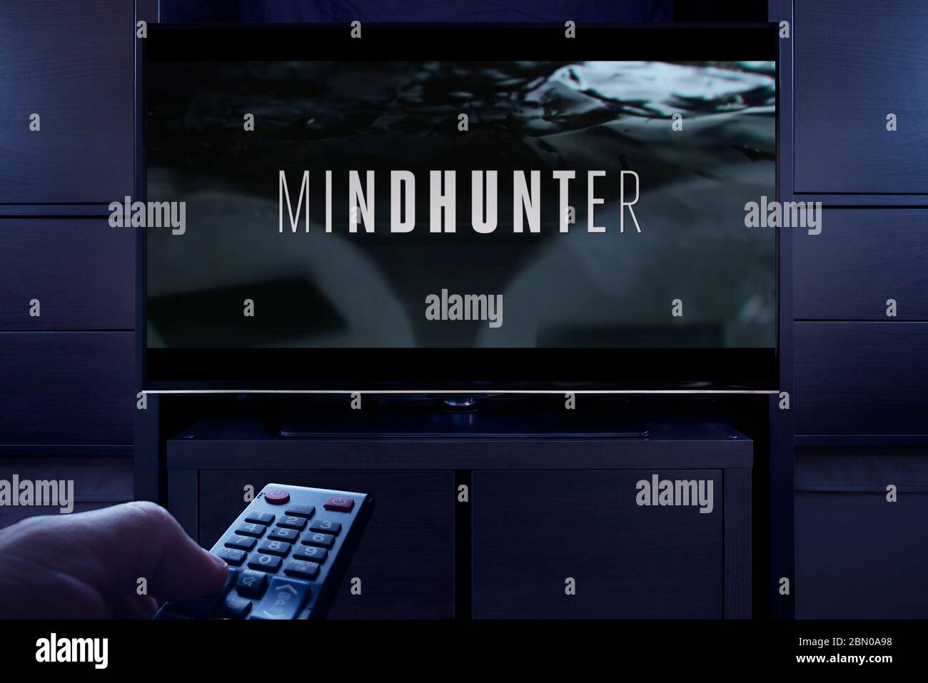 Ein Mann zeigt eine TV-Fernbedienung auf den Fernseher, der den Mindhunter Haupttitelbildschirm anzeigt (nur redaktionelle Verwendung). Stockfoto