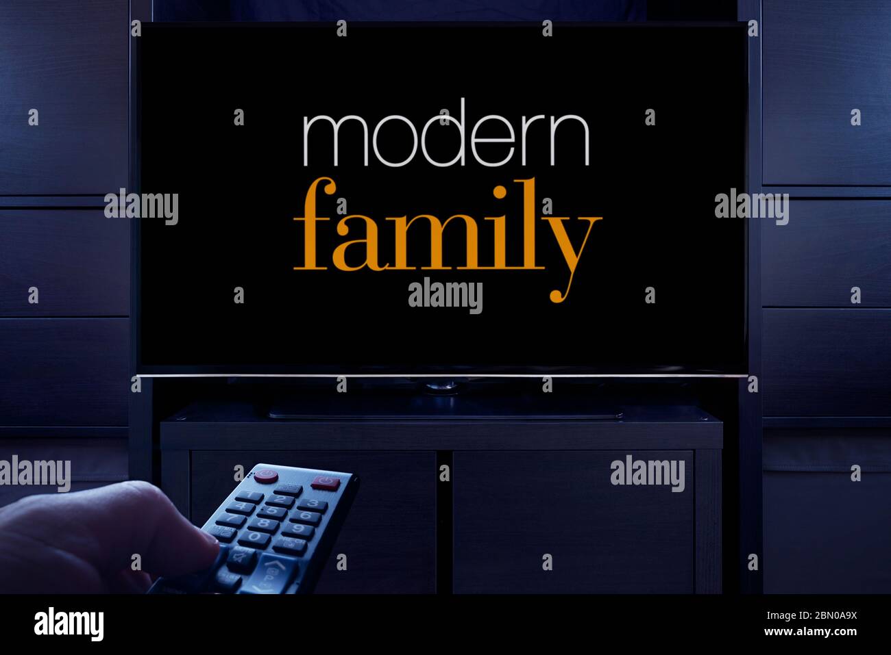 Ein Mann zeigt eine Fernbedienung auf den Fernseher, der den Hauptbildschirm der Modern Family anzeigt (nur redaktionelle Verwendung). Stockfoto