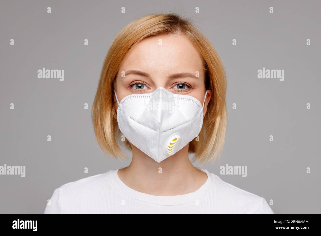 Studio-Porträt einer jungen Frau, die eine Gesichtsmaske trägt, die Kamera anschaut, Nahaufnahme, isoliert auf grauem Hintergrund. Grippeepidemie, Stauballergie, Schutz Stockfoto