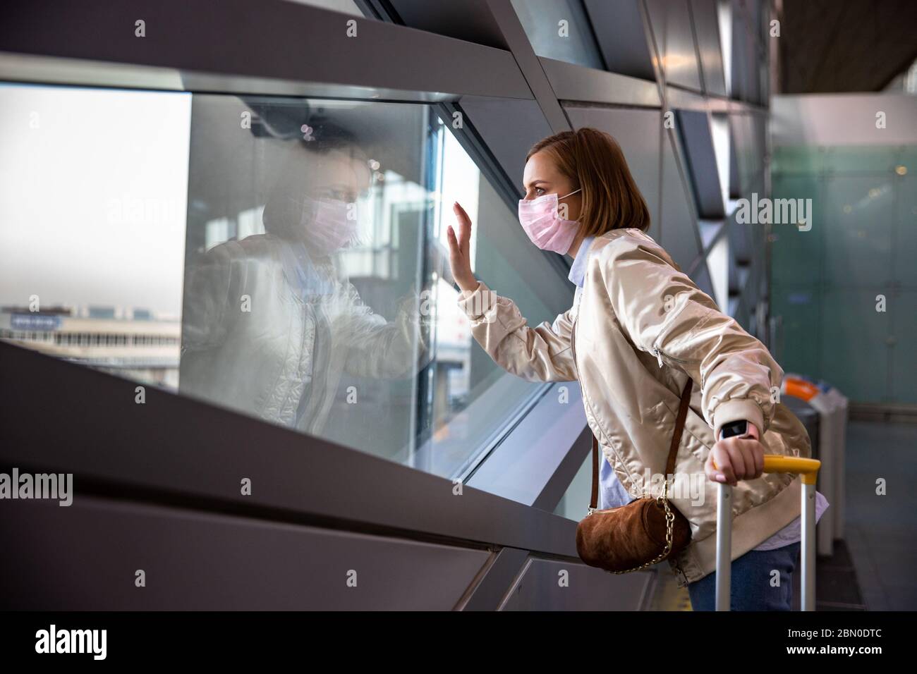 Traurige Frau, die eine medizinische Gesichtsmaske trägt und auf das Fenster am fast leeren Flughafenterminal schaut, das wegen der Coronavirus-Pandemie, dem Ausbruch von Covid-19, verursacht wurde Stockfoto