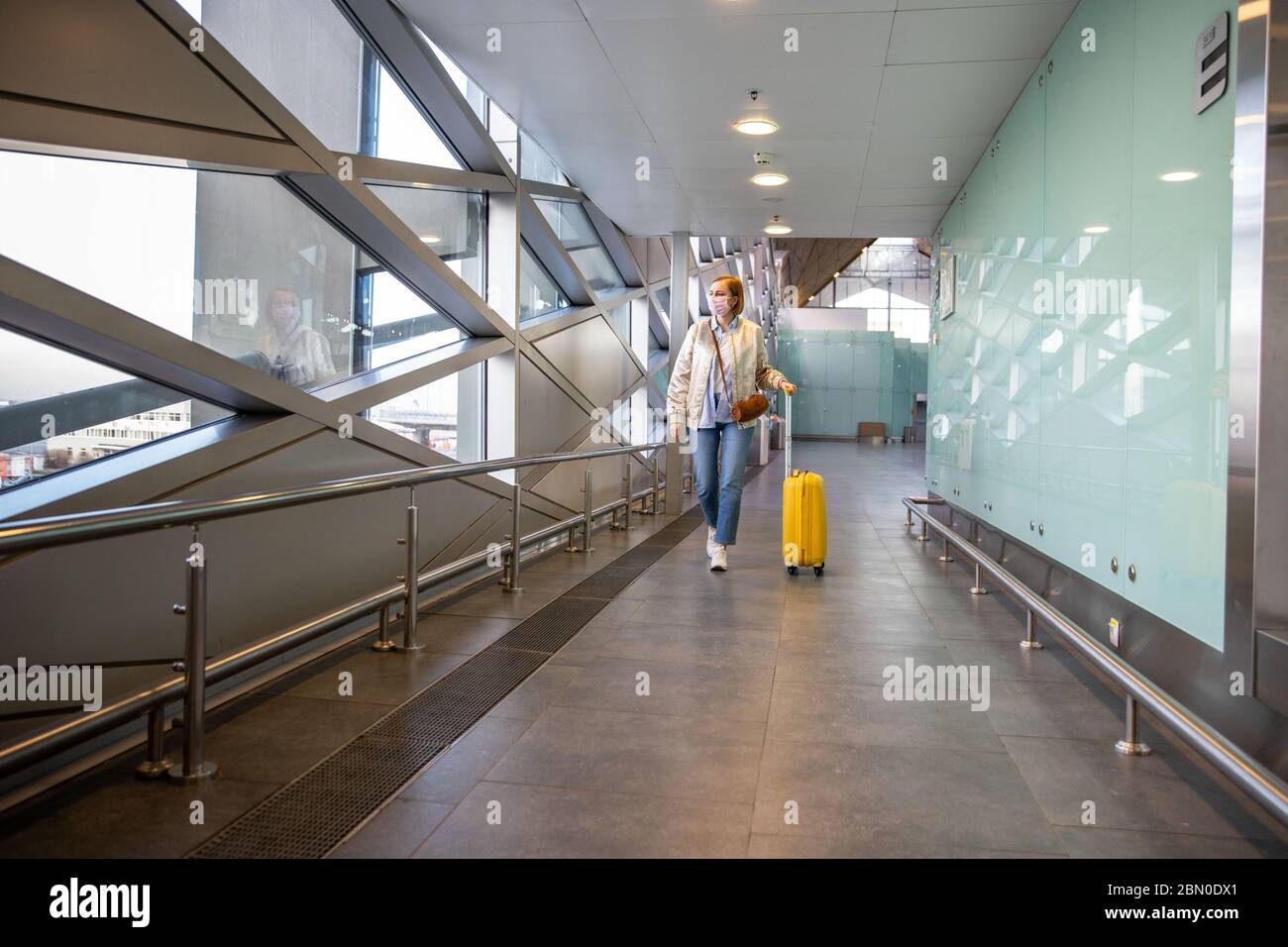 Passagierin Frau mit einer medizinischen Schutzmaske zur Verhinderung Coronavirus zu Fuß mit ihrem Gepäck in fast Flughafen / Reisestation. Reise BA Stockfoto