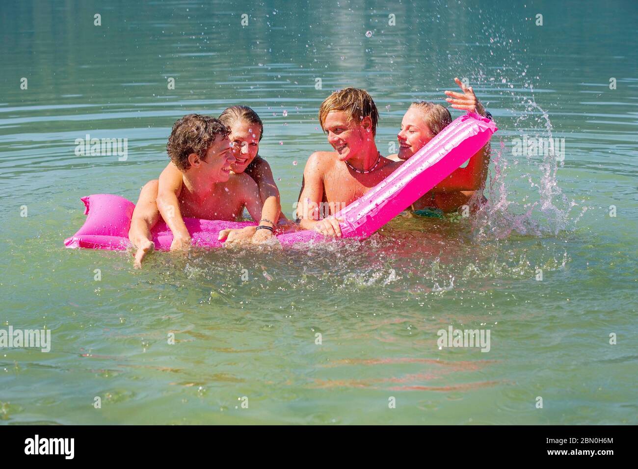 Vier Jugendliche auf einer Luftmatratze im Wasser haben Spaß am Baden, 18 Jahre, Mondsee, Oberösterreich, Österreich Stockfoto