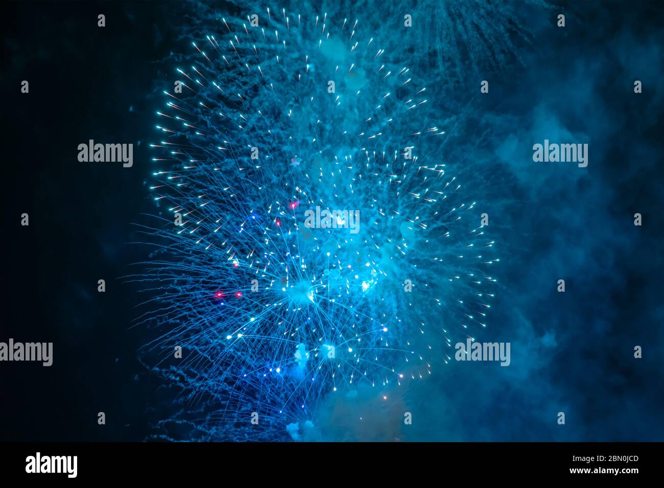Blau-weißes Feuerwerk mit Rauch über dem schwarzen Himmel. Geringe Tastenbelichtung. Selektiver Fokus. Stockfoto