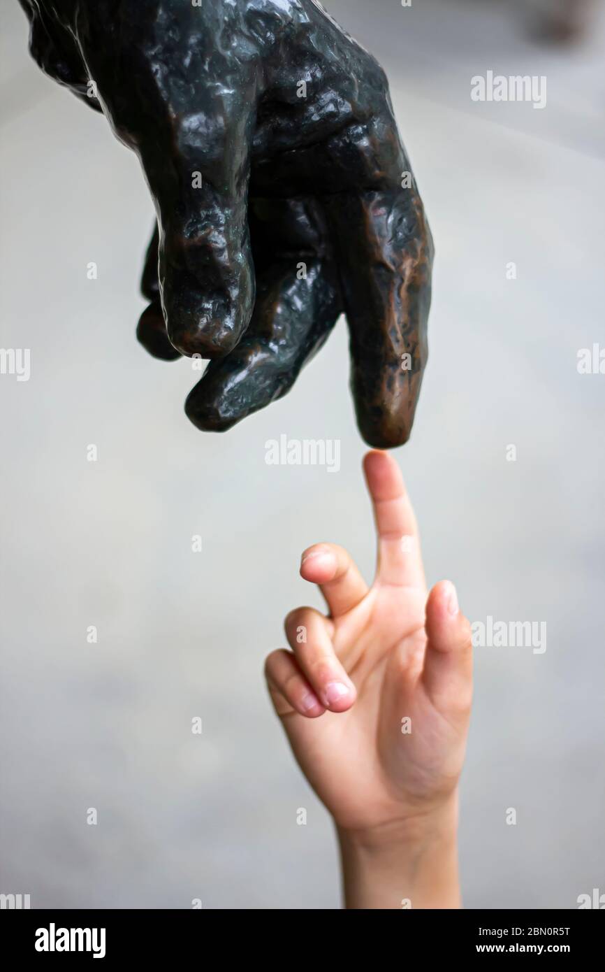 Eine menschliche Hand berührt Finger an Finger mit einer Statue wie Michelangelo und seinem berühmten Gemälde von Gott und Mensch Schöpfung Stockfoto