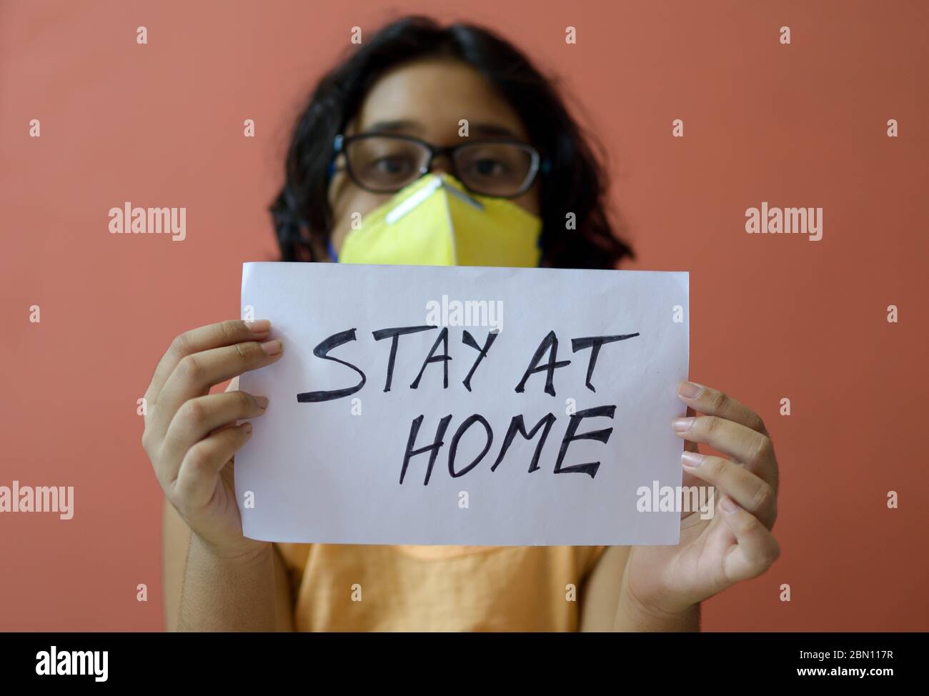 Kleines indisches Mädchen mit Gesichtsmaske hält ein Plakat in den Händen und zeigt eine Botschaft "Stay at Home" während der COVID-19 Pandemie, um soziale Distanz zu erhalten. Stockfoto