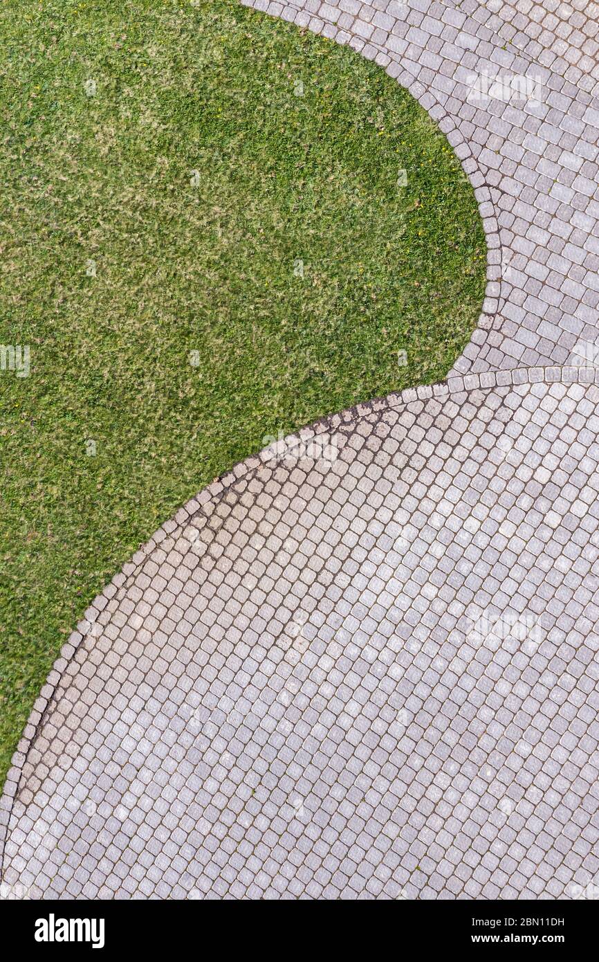 Draufsicht auf grauen gepflasterten Gehweg mit grünen Gras Textur um Steine Stockfoto