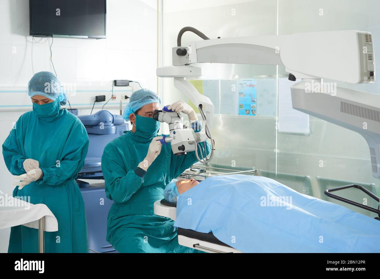 Chirurg, der den ophthalmischen Laser über dem Kopf des Patienten anpasst, wenn er Gummihandschuhe anlegt Stockfoto