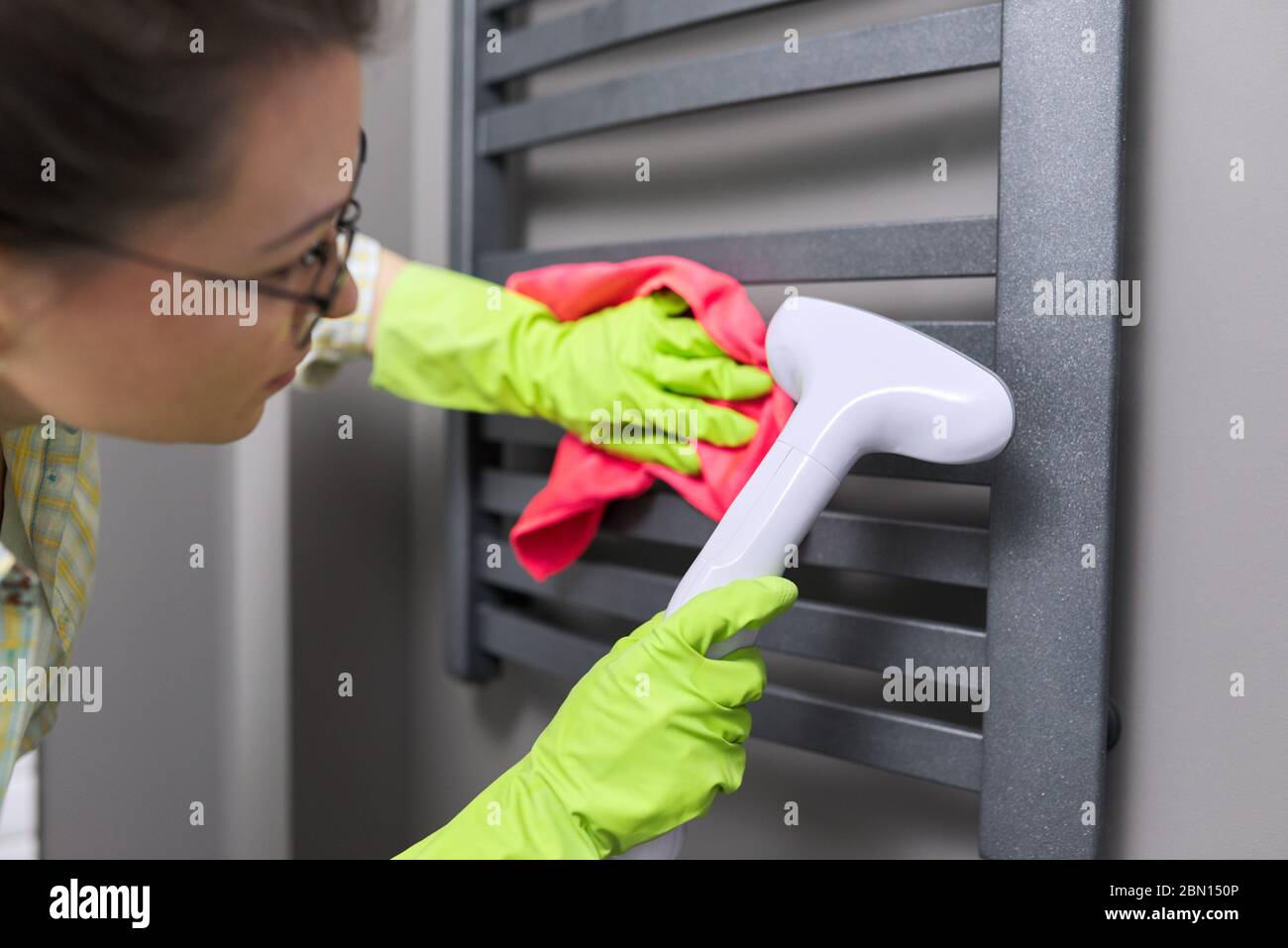 Frau, die die beheizte Handtuchschiene mit Dampfmaschine reinigt Stockfoto