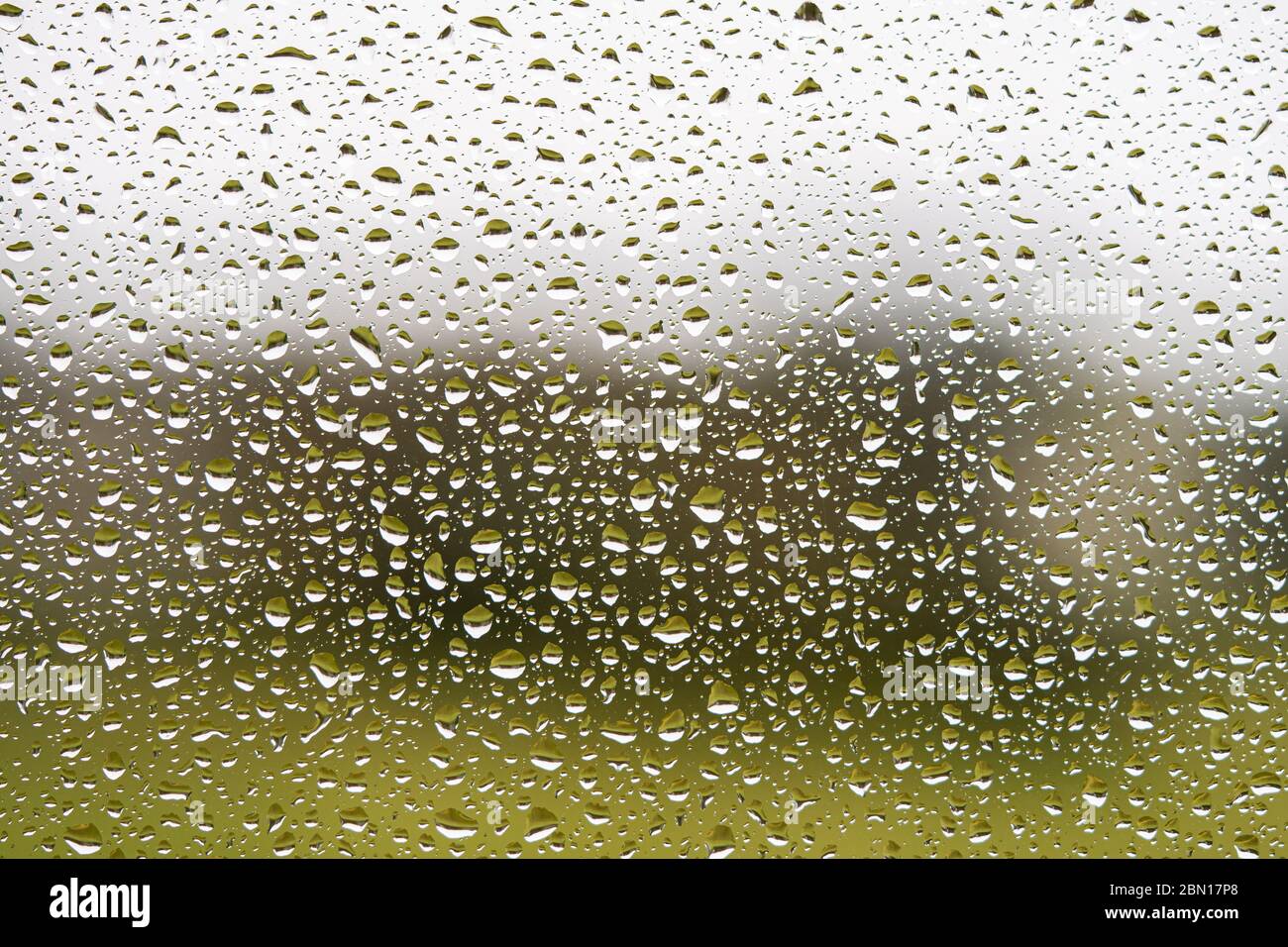 Regentropfen auf Glasfenster. Dunkelgrauer und grüner strukturierter Hintergrund. Vollformat Makro Foto. Stockfoto