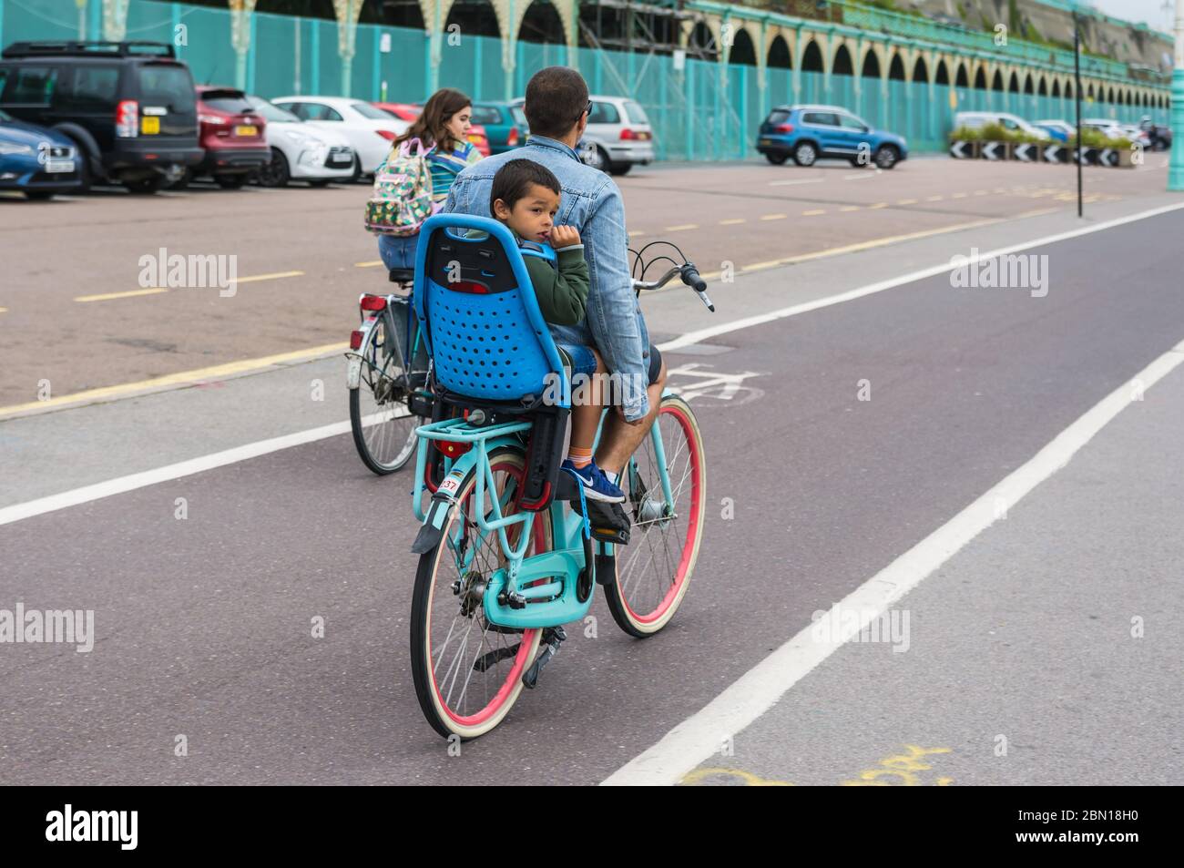 Kinder, die in Großbritannien auf einem Kindersitz auf der Rückseite eines Fahrrads fahren, ohne einen Sicherheitshelm zu tragen. Stockfoto