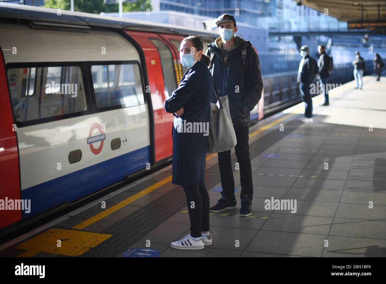 Passagiere tragen Gesichtsmasken auf einem Bahnsteig an der U-Bahn-Station Canning Town in London. Stockfoto