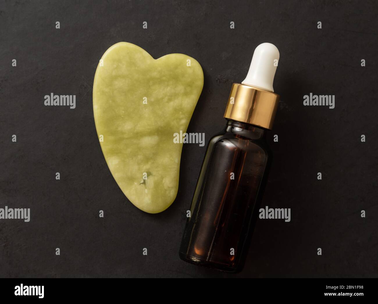 Gua Sha Werkzeug mit Glasflasche Serum bei schwarzem Backgorund. Massage mit gua Sha Konzept Stockfoto