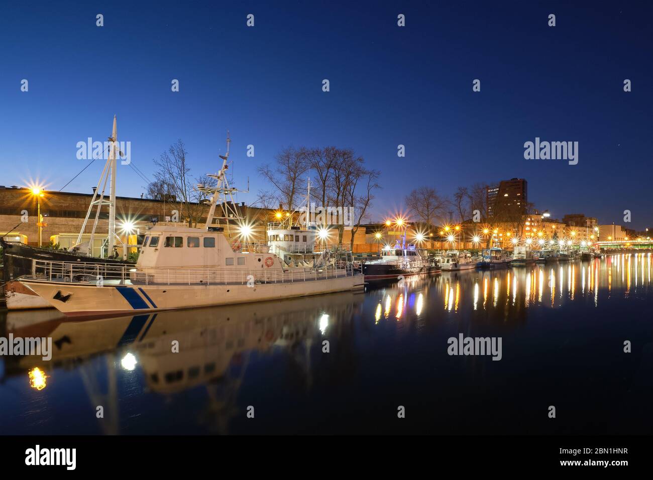 Pier für Boote und Yachten in Klaipeda, Litauen, bei Sonnenuntergang. Schöne Sicht auf Schiffe und ihre Reflexionen in ruhigem Wasser auf blaue Stunde Stockfoto