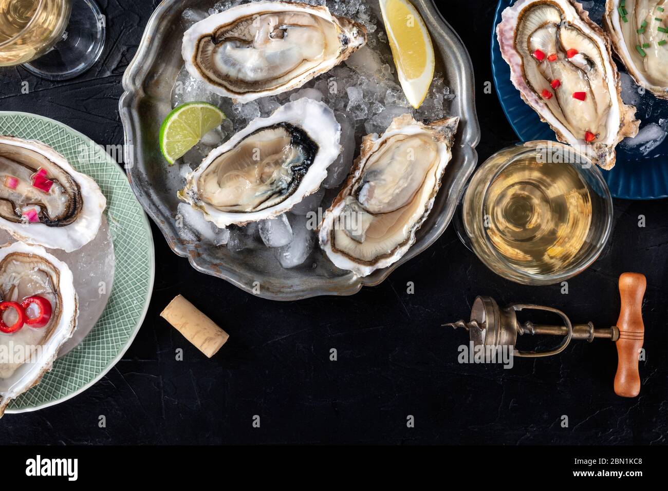 Austern mit verschiedenen Belägen, von oben mit Wein, mit Zitrone und Limette, Pfeffer, Zwiebel, auf dunklem Hintergrund mit einem Platz für Text erschossen Stockfoto