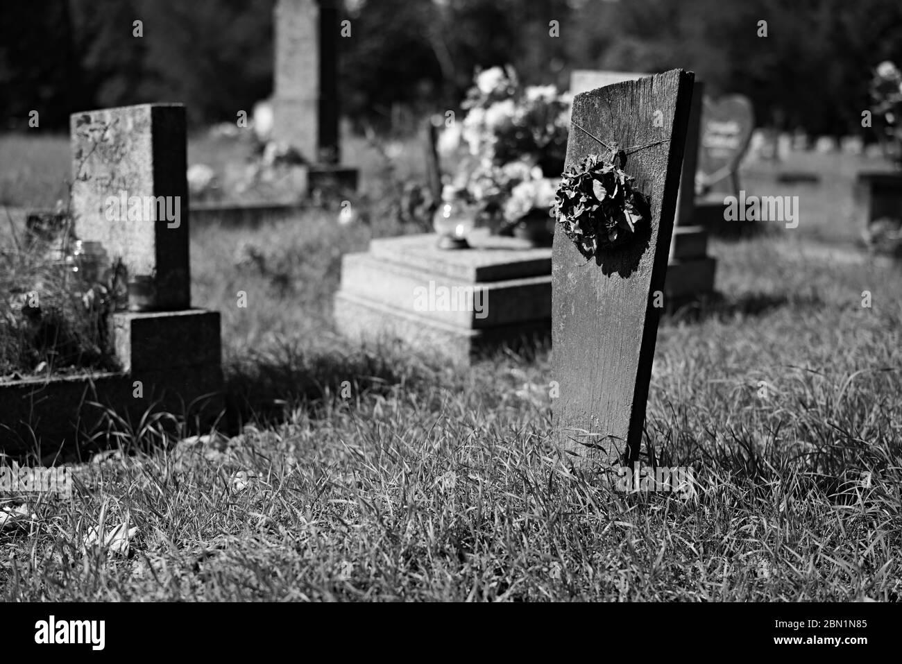 Improvisierter Holzgrabstein, der den Elementen lange Zeit ausgesetzt war, dekoriert mit trockenem Kranz auf namenlos vergessenem Grab auf dem örtlichen Friedhof. Stockfoto