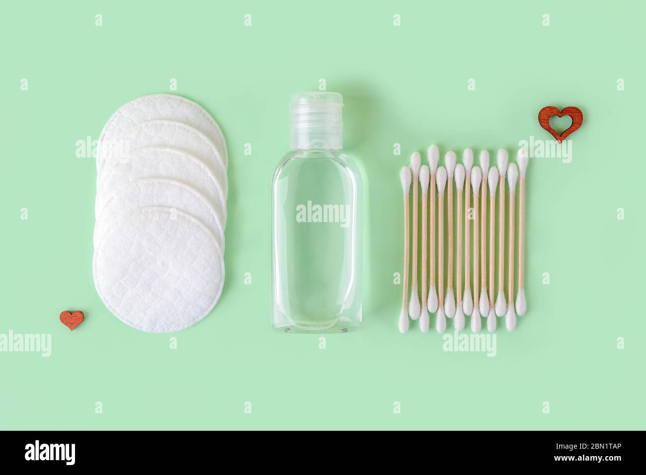 Reinigungslotion oder Tonic in einem transparenten Glas, Wattepads und Wattestäbchen Holzstick auf einem pastellfarbenen Minze-Hintergrund. Konzept der umweltfreundlichen Materialien Stockfoto