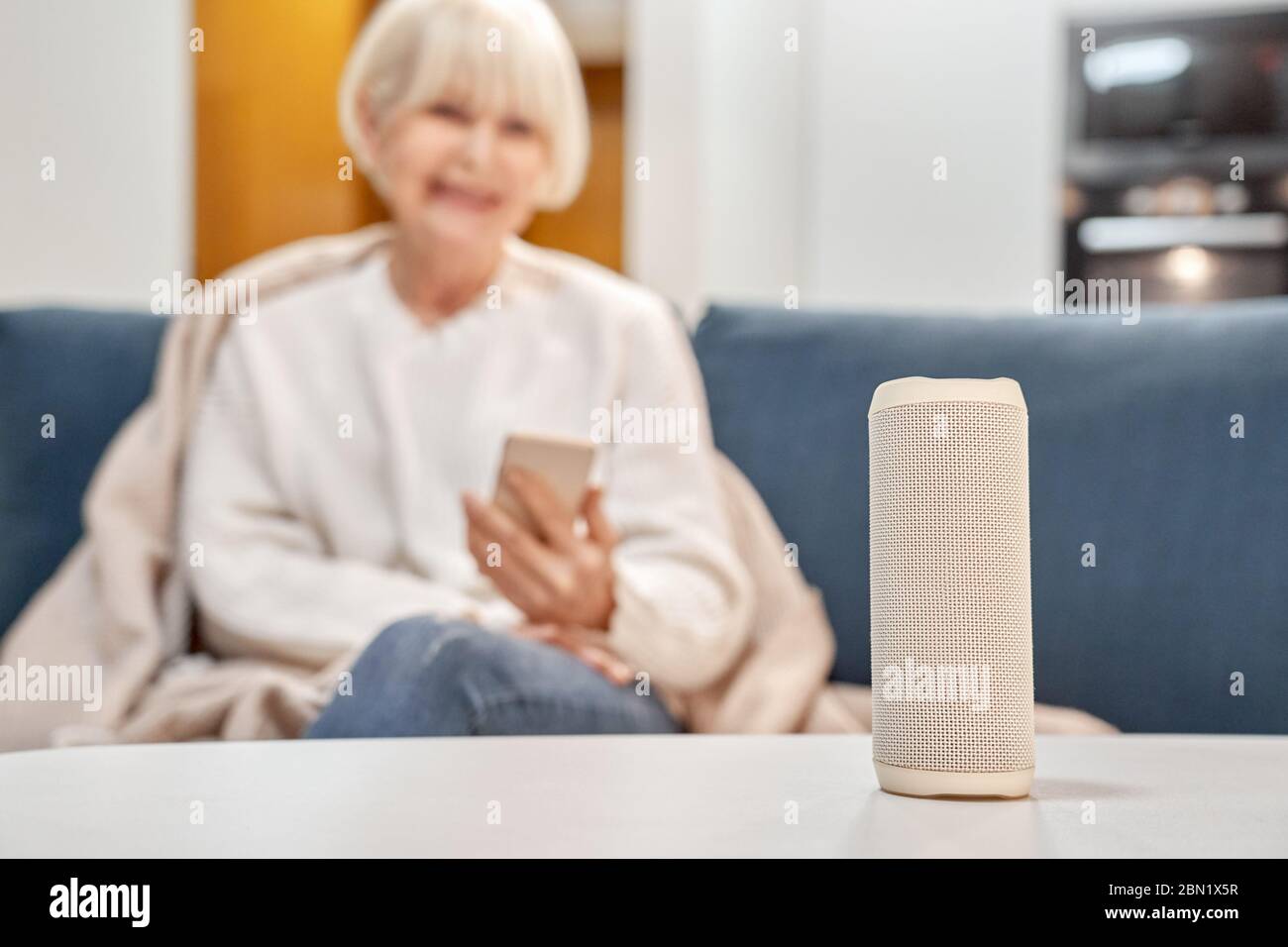 Ruhestandsfrau sitzt in der Nähe von Smart-Lautsprecher und drahtlose digitale Assistent Stockfoto