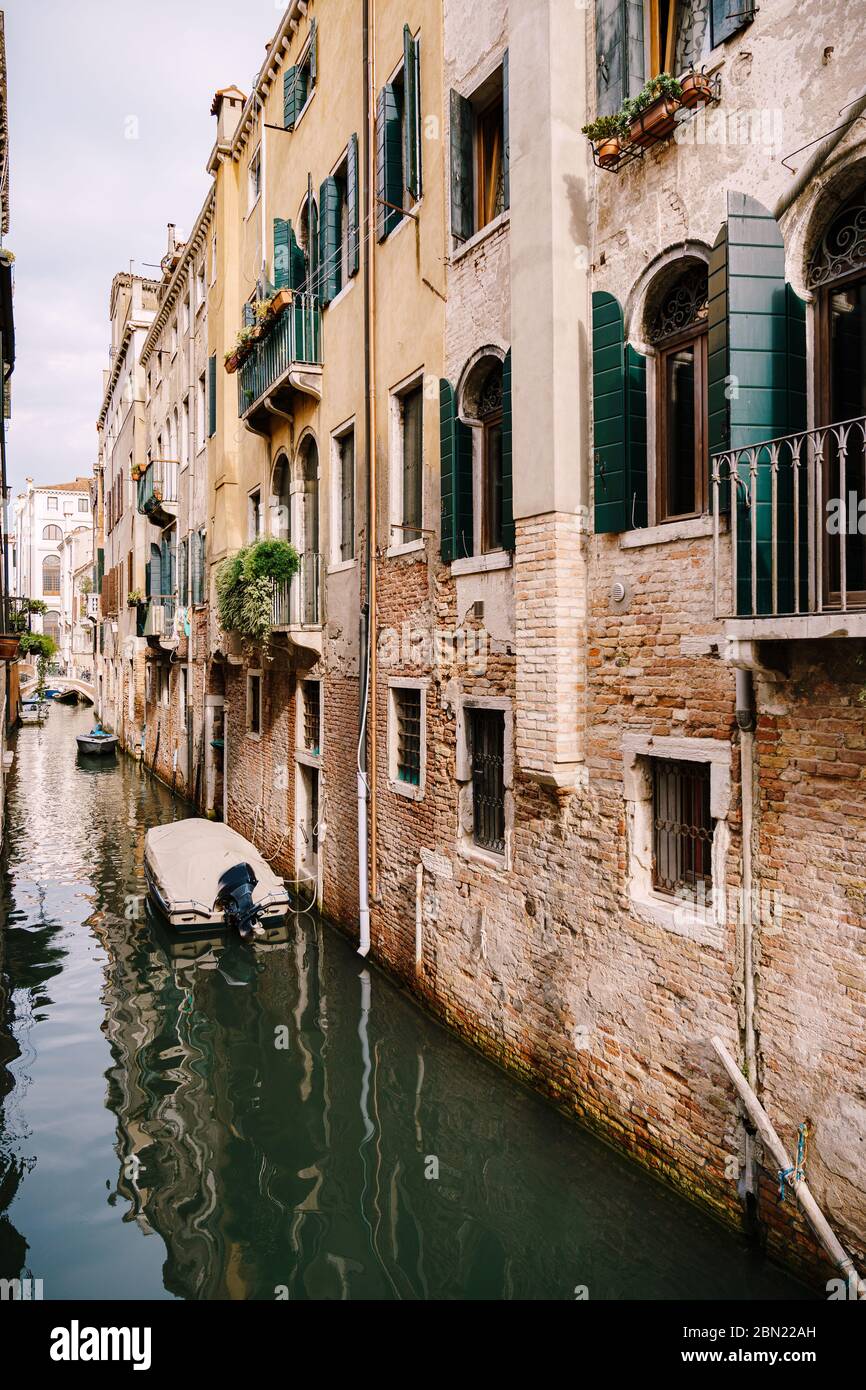 Boote vor den Mauern von Häusern im Wasser in Venedig. Enge verlassene Kanal zwischen Häusern, azurblaues Meerwasser am Fuße des Hauses. Stockfoto