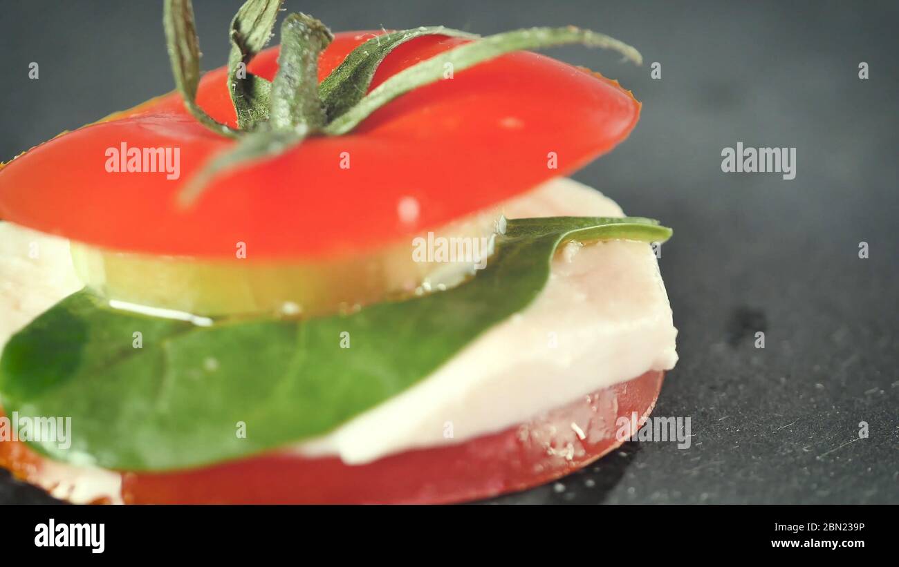 Salat aus Turmkaprese. Gesunder vegetarischer Salat mit geschnittenen Tomaten, Gurken, Mozzarella und Basilikum. Frisches, natürliches Sommerdinner. Dunkle Platte. Nahaufnahme Stockfoto