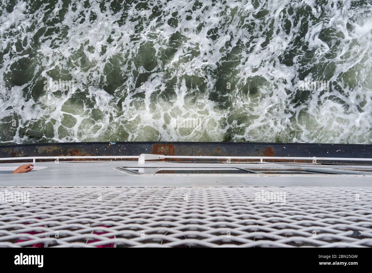 Blick nach unten auf eine Person Hand hängt aus einem Schiff mit dem schäumenden Wasser unten Stockfoto