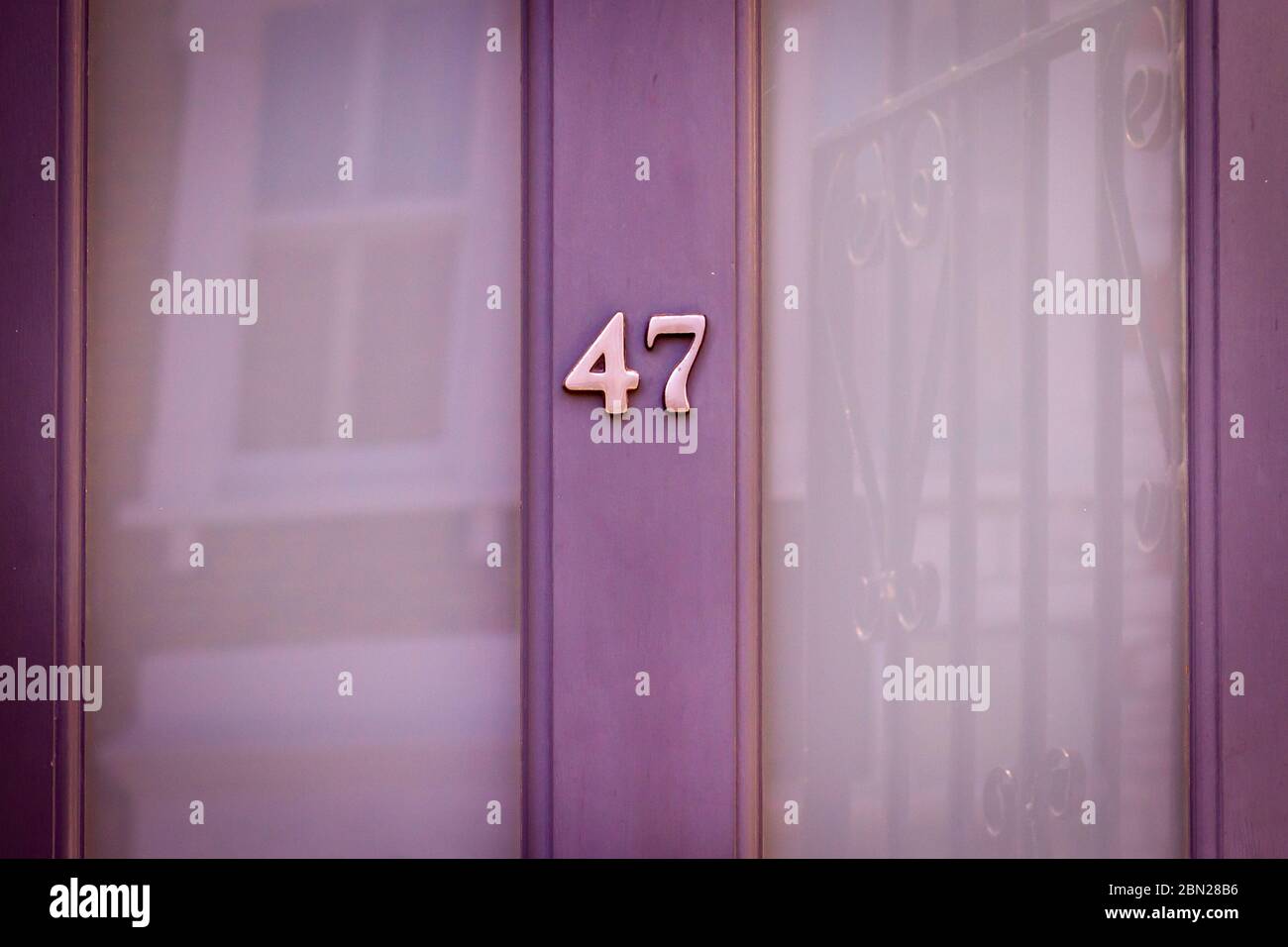 Haus Nummer 47 auf einer hellvioletten Holztür mit großen Glasfenstern, die ein Haus gegenüber reflektieren Stockfoto