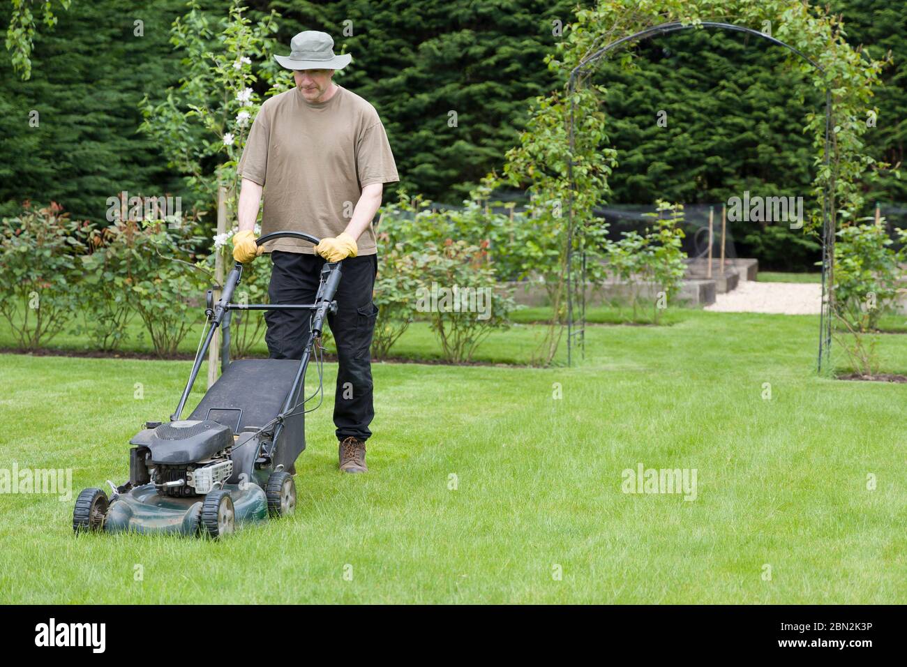 Mann oder Gärtner mähen einen Rasen in einem Garten im Sommer mit einem Rasenmäher, Großbritannien Stockfoto