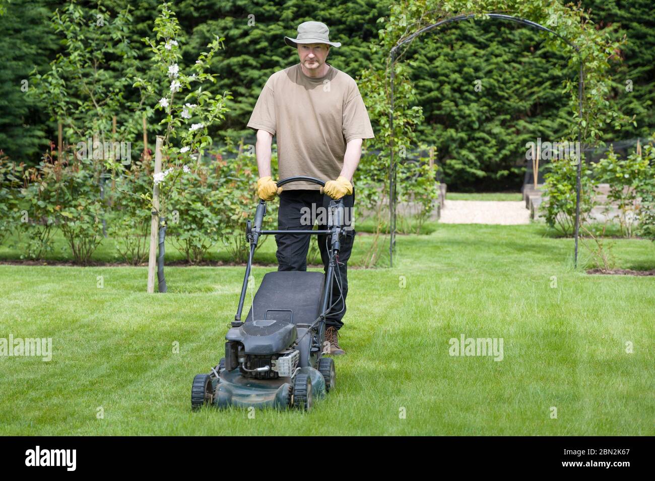 Mann mäht einen Rasen auf dem Gelände eines Luxushauses, Rasenpflege und Rasenpflege, Großbritannien Stockfoto