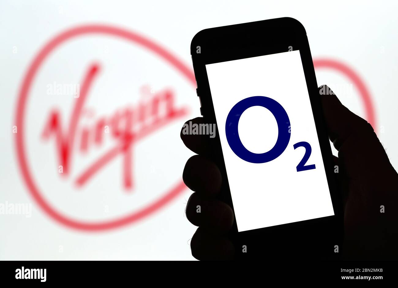o2-Mobilfunknetz-Logo auf einem Mobiltelefon mit dem Virgin Media-Logo dahinter. (Nur redaktionelle Verwendung) Stockfoto