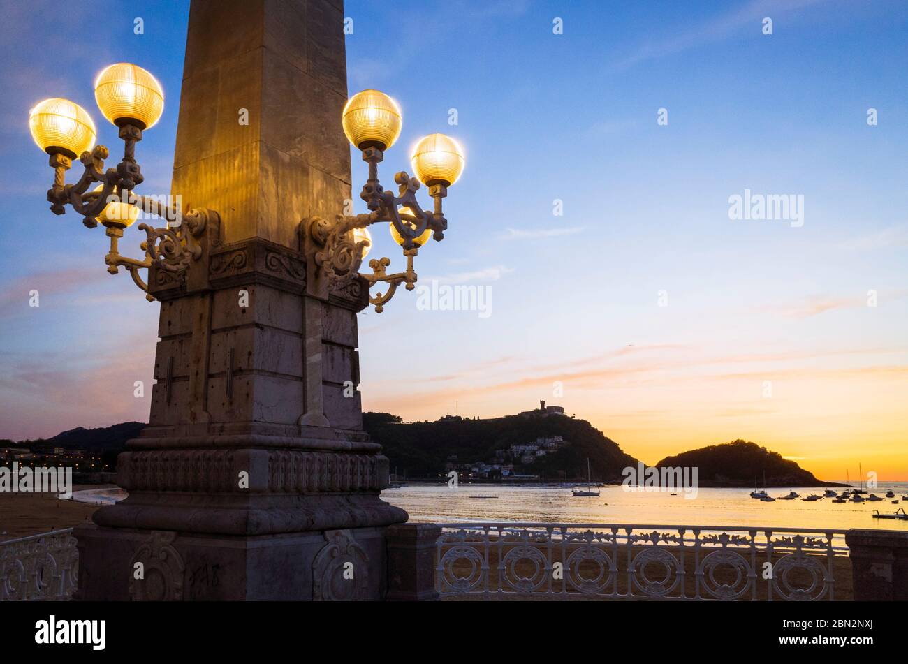 San Sebastian, Gipuzkoa, Baskenland, Spanien: La Concha Strand und ikonische Straßenlampe bei Sonnenuntergang beleuchtet. Stockfoto