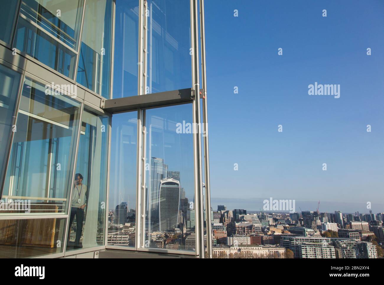 Geschäftsmann, der am sonnigen Bürofenster in einem Hochhaus Smartphone benutzt Stockfoto