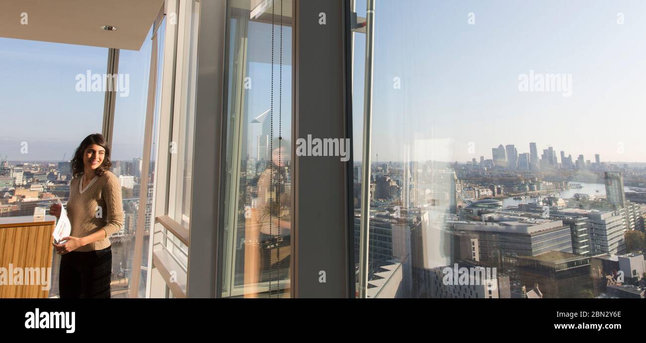 Lächelnde Geschäftsfrau in sonnigen städtischen Hochhaus Bürofenster Stockfoto
