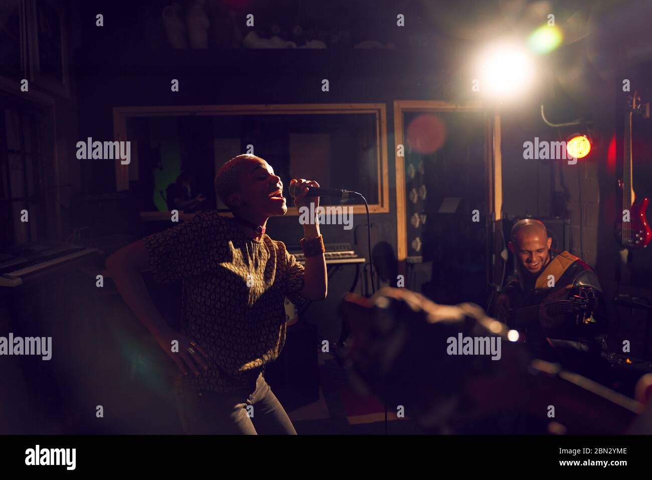 Musikerin singt ins Mikrofon im dunklen Aufnahmestudio Stockfoto