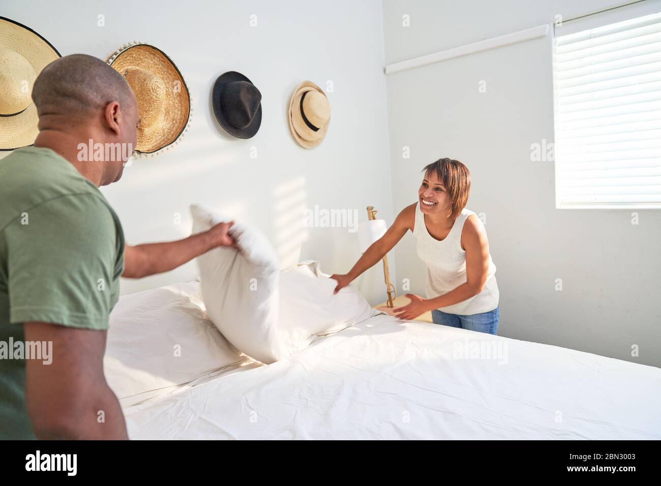 Glückliches Paar, das Bett im sonnigen Schlafzimmer machte Stockfoto