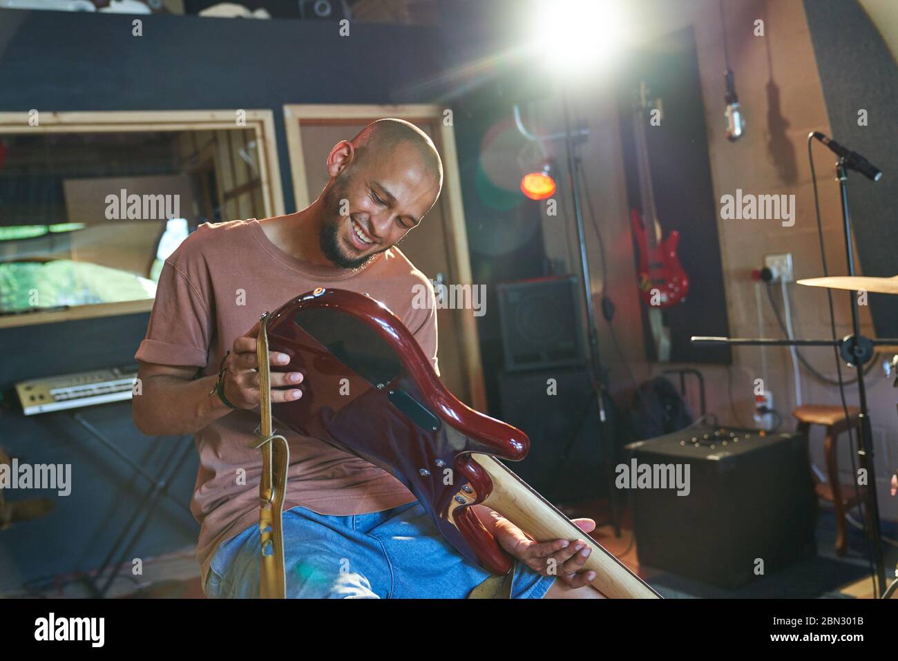 Lächelnder männlicher Musiker, der Gitarre im Aufnahmestudio inspiziert Stockfoto