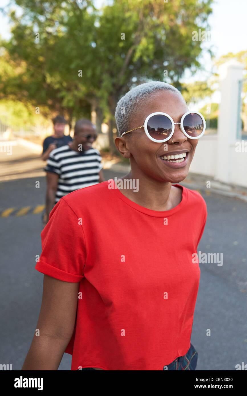 Glückliche junge Frau in Sonnenbrille zu Fuß in der Straße Stockfoto
