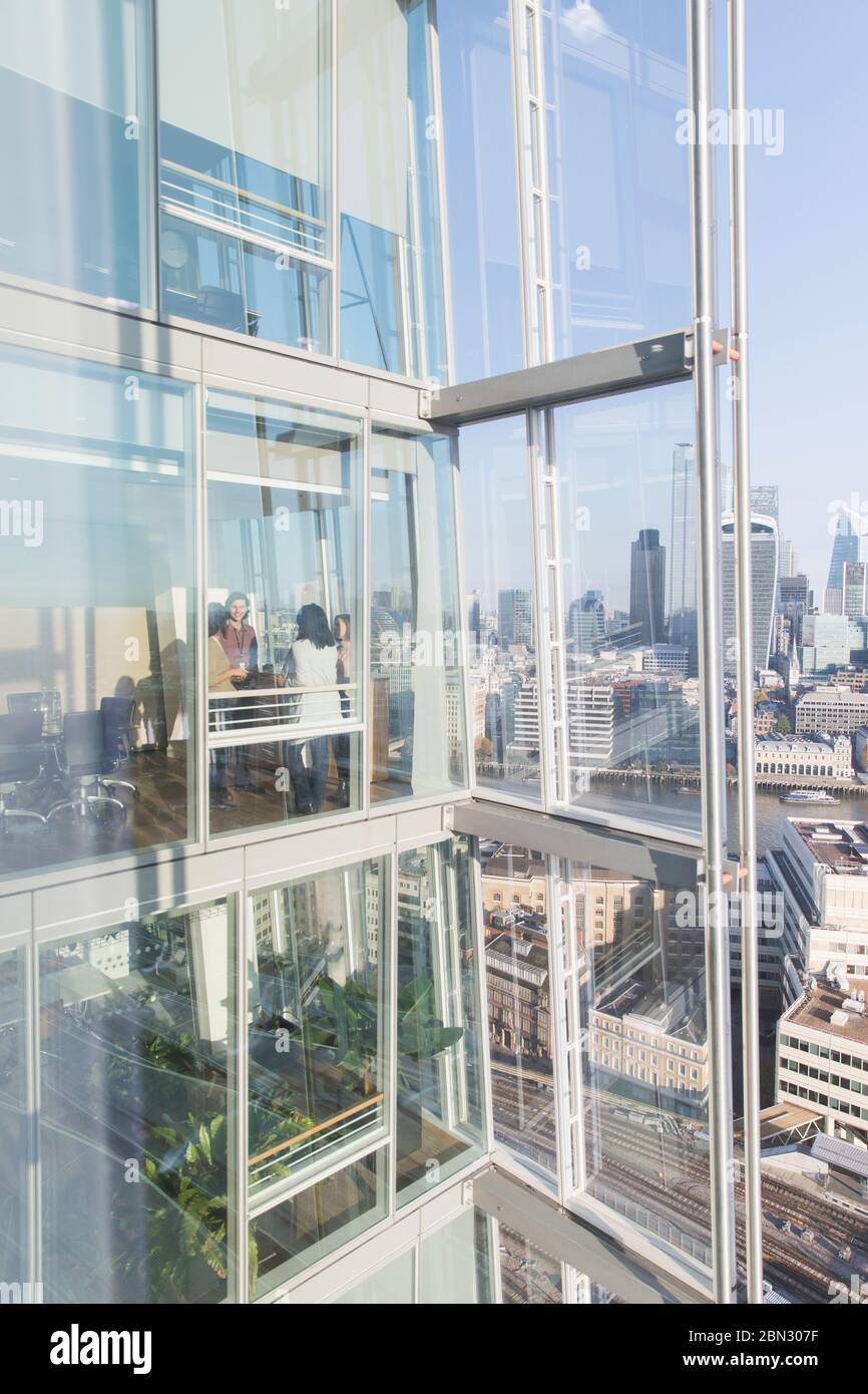 Geschäftsleute sprechen im sonnigen, modernen Hochhaus-Bürofenster Stockfoto
